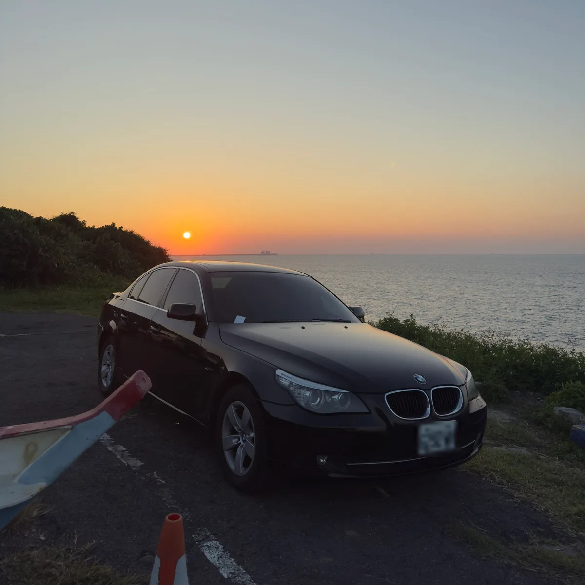 黑色 BMW E60 520d 停在海邊的觀景平台，前方是日落中的海平面