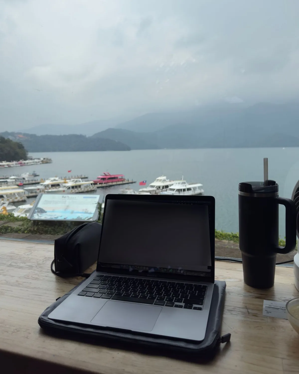 面湖吧台桌上的 MacBook，窗外是日月潭與碼頭遊艇