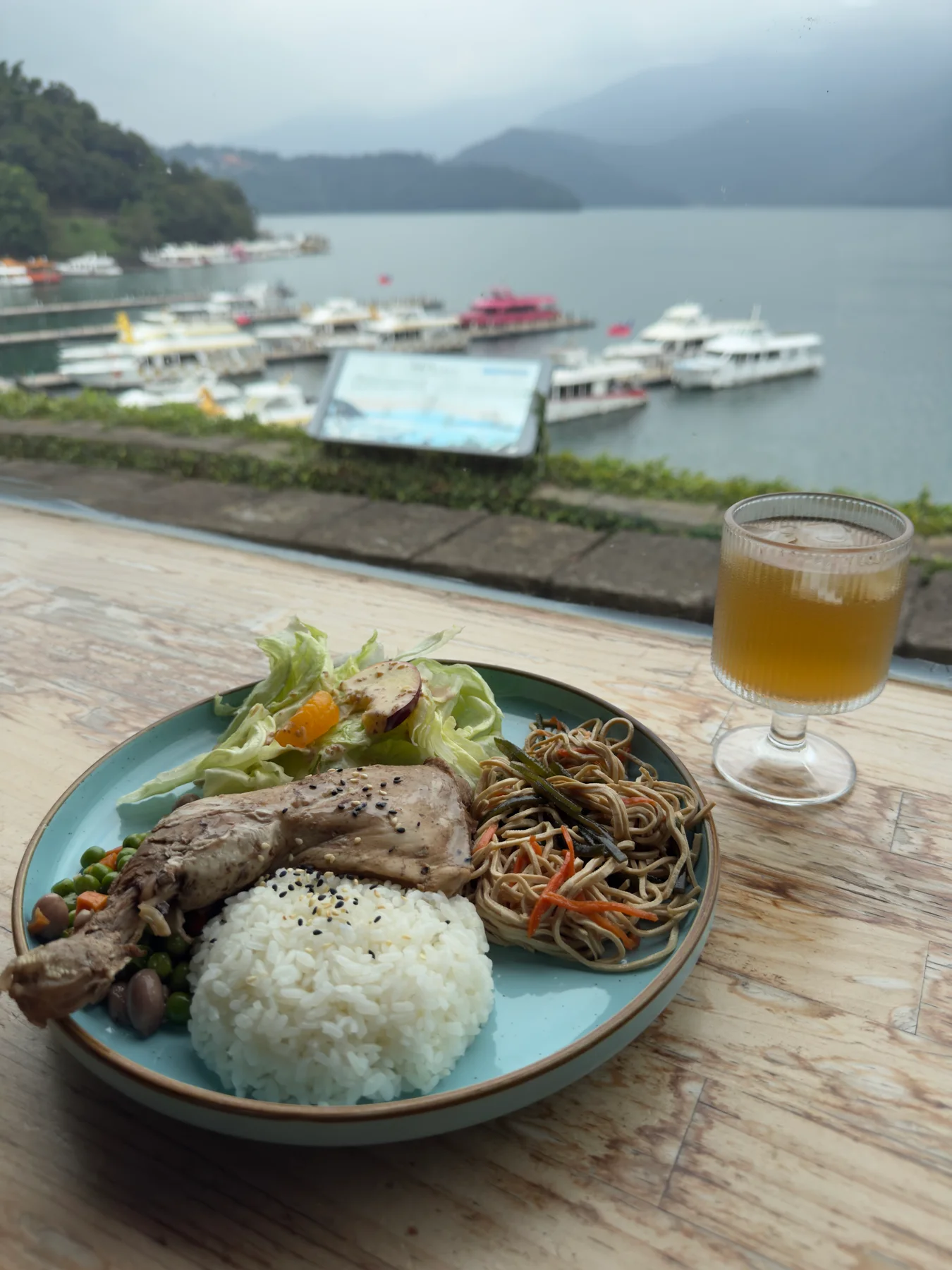 窗邊木桌上的雞腿飯與無糖麥茶，後方是日月潭碼頭