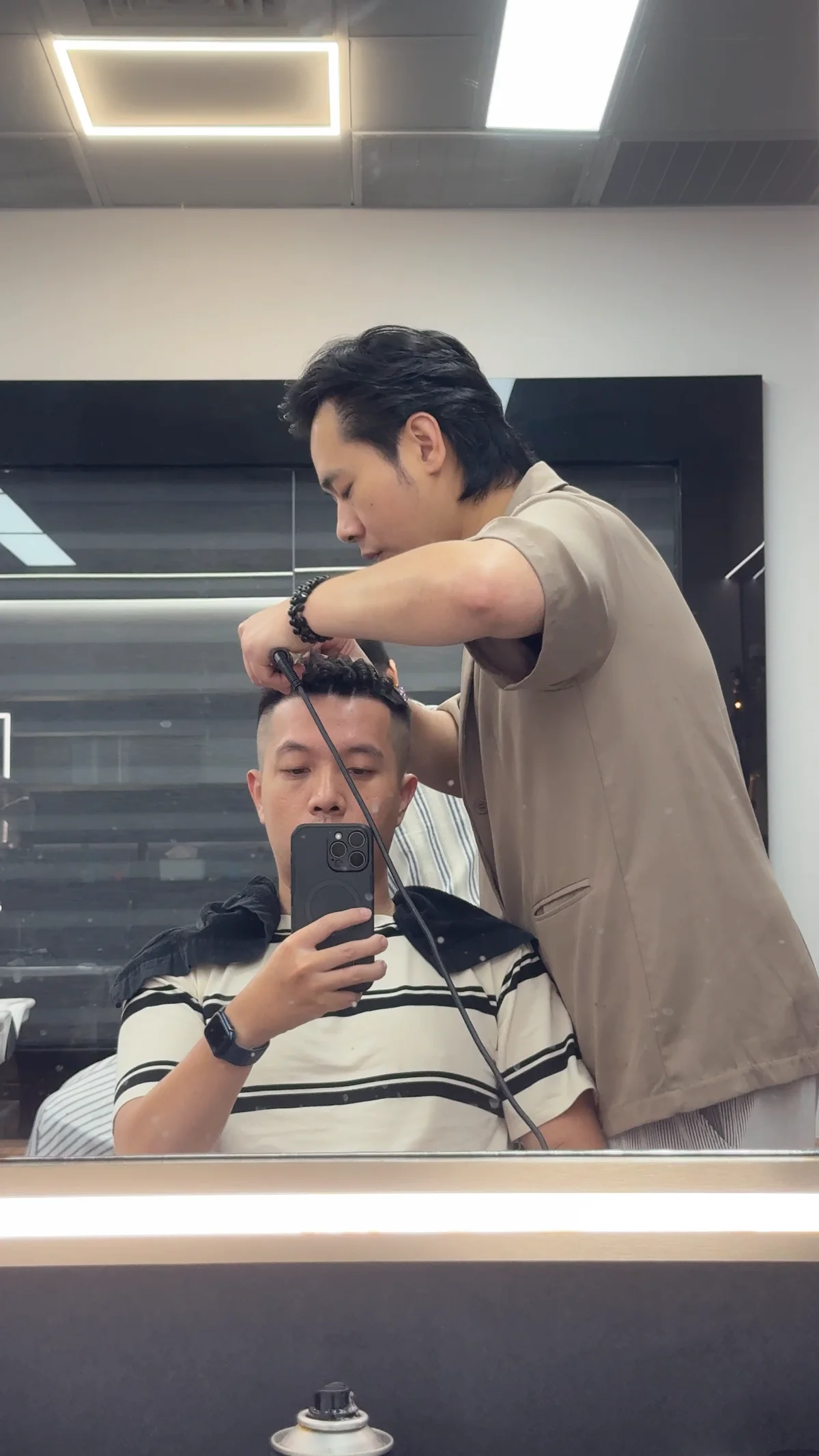 鏡子裡理髮師站在身後修剪頭髮，手上拿著剪刀