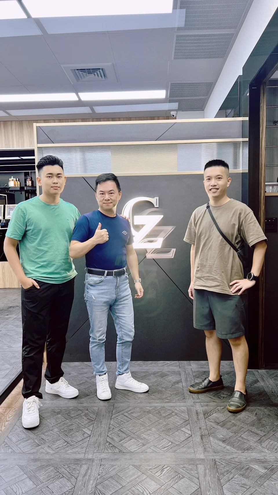 三個人站在店內的 GZ 標誌牆前合照，右邊是我